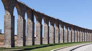 A long stone aqueduct with arches, a paved road alongside, and a clear sky.