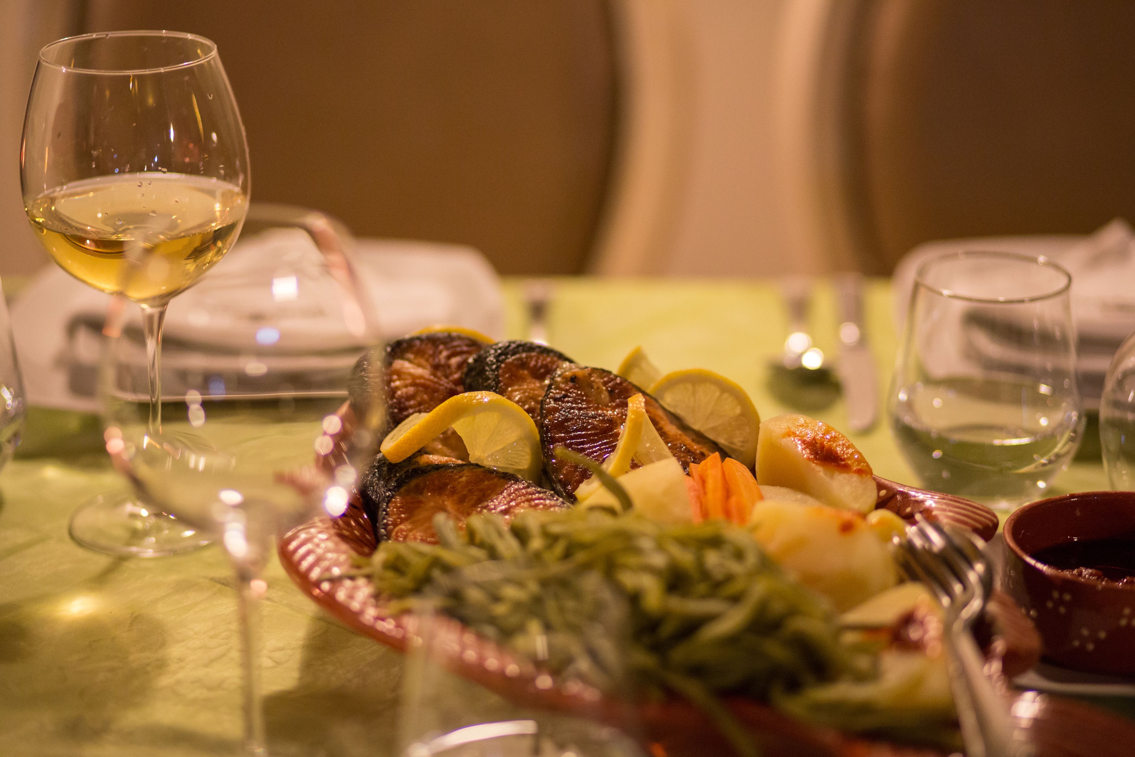 A dining table with a plate of food, a glass of white wine, and a bowl of sauce.
