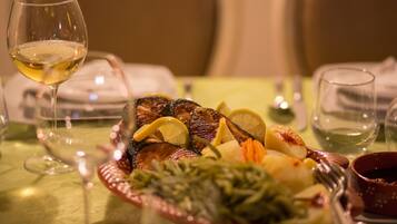 A dining table with a plate of food, a glass of white wine, and a bowl of sauce.