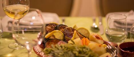 A dining table with a plate of food, a glass of white wine, and a bowl of sauce.