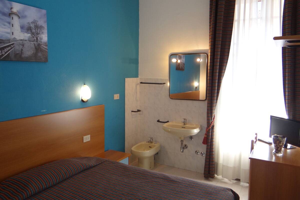 A hotel room with a bed, a bedside table, a sink, and a mirror.