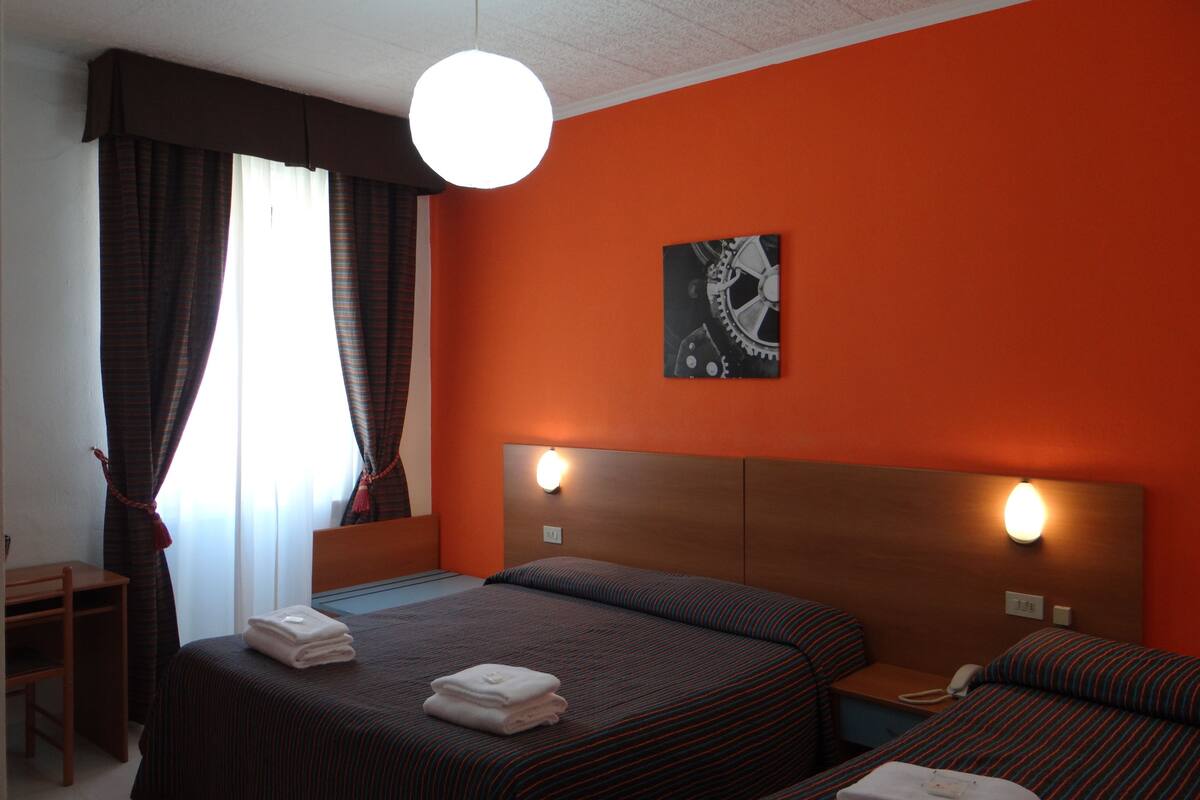 A hotel room with two beds, a wooden nightstand, a desk, and a wall-mounted clock.