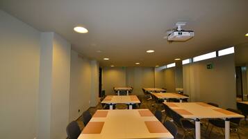 A conference room with multiple tables and chairs, a ceiling-mounted projector, and a carpeted floor.