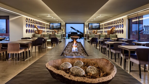 A modern interior with a central fire feature, dining tables, chairs, and a wall of decorative plates. - Vitória Stone Hotel (Évora)