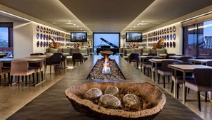 A modern interior with a central fire feature, dining tables, chairs, and a wall of decorative plates. - Vitória Stone Hotel (Évora)
