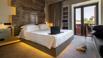 A modern hotel room with a large bed, a laptop on the bed, a desk with a chair, and a view of the outdoors through a sliding door.
