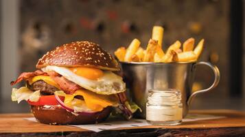 A burger with fries and a small jar of sauce on a wooden table.
