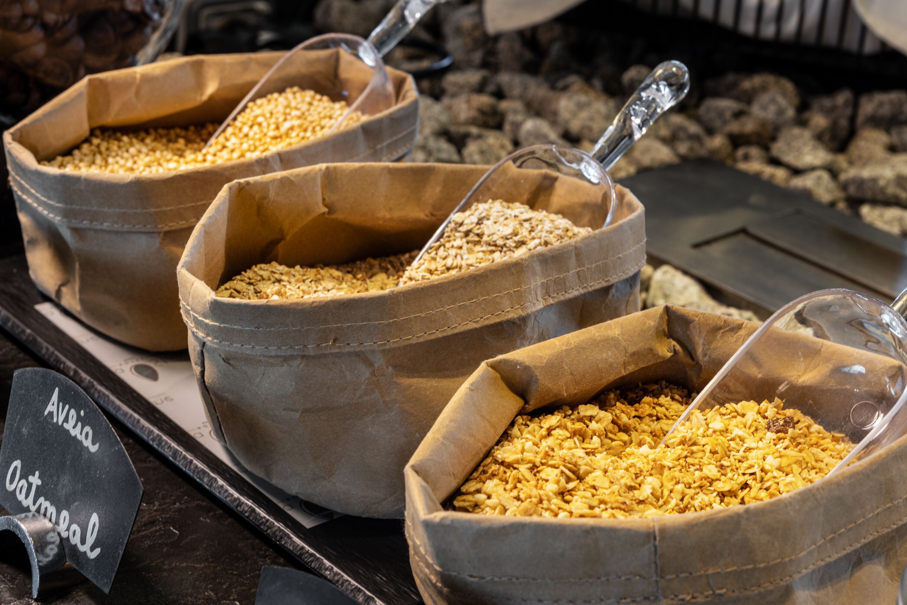 Kolme kaurapussia, joiden etiketissä lukee ”Avena Oatmeal”, on asetettu puupinnalle.
