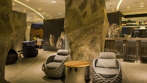 A modern lounge area with cushioned seating, a central round table, and a bar in the background. - Vitória Stone Hotel (Évora)