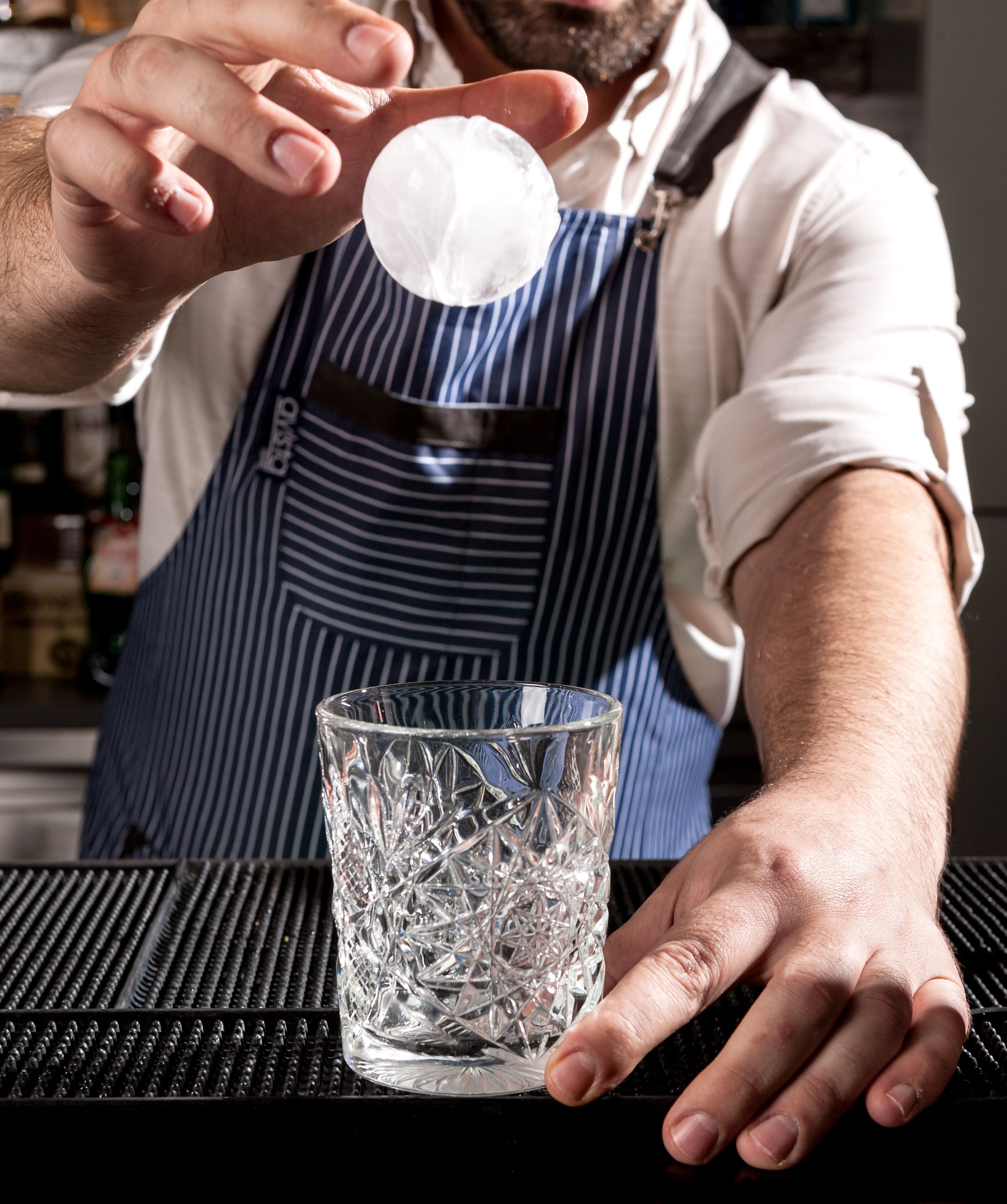 Una persona sosteniendo un cubito de hielo transparente sobre un vaso.