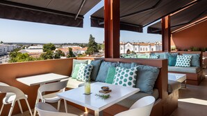 An outdoor seating area with a view of the city, featuring a table, chairs, and a sofa with patterned cushions. - Vitória Stone Hotel (Évora)
