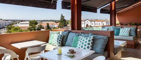 An outdoor seating area with a view of the city, featuring a table, chairs, and a sofa with patterned cushions.