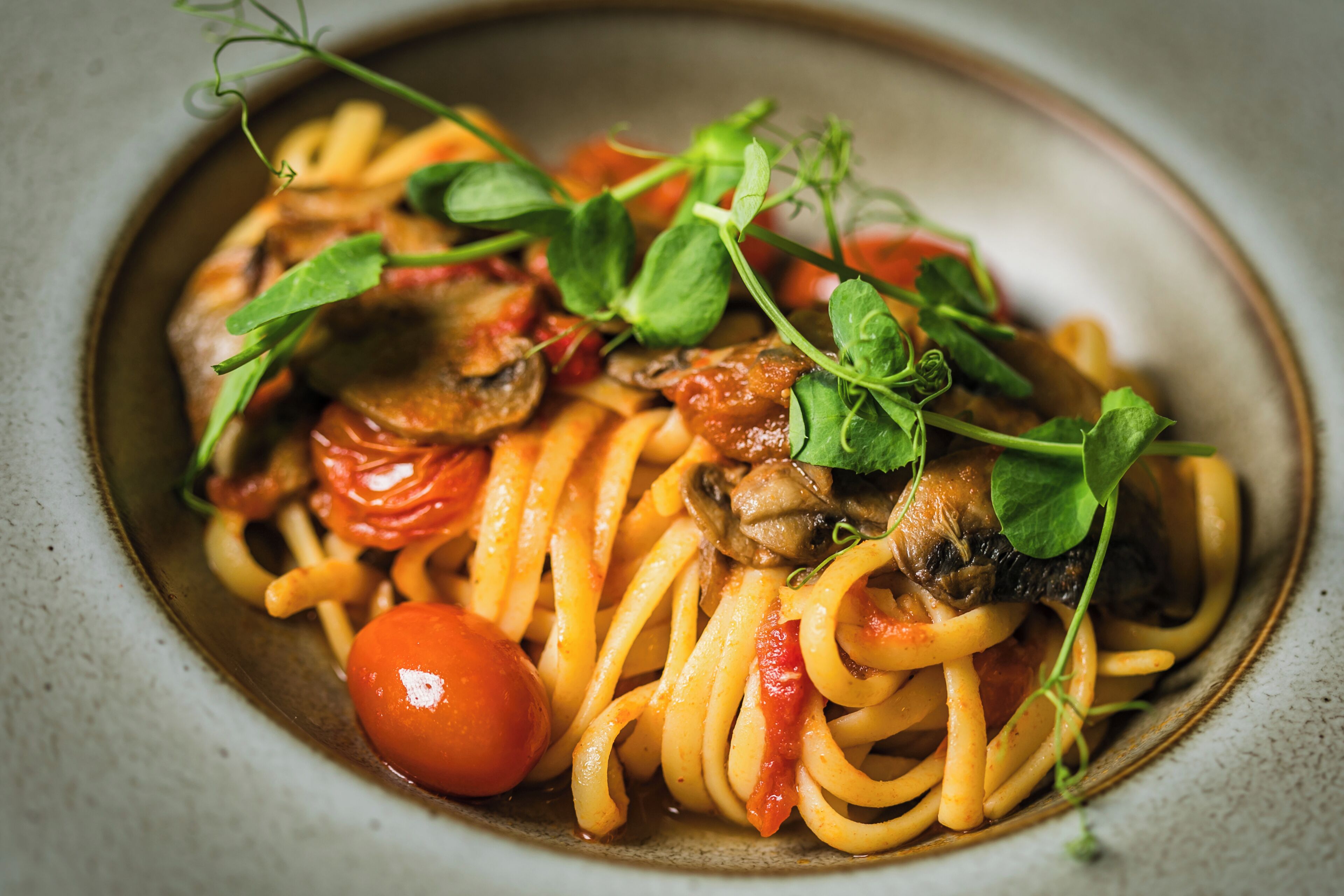 A plate of spaghetti with tomatoes and mushrooms, garnished with green leaves.