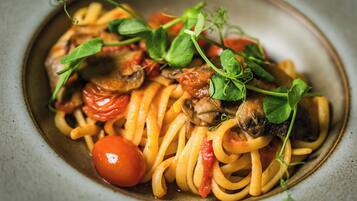 A plate of spaghetti with tomatoes and mushrooms, garnished with green leaves.
