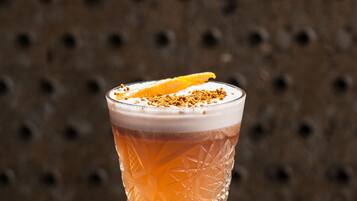 Una copa de cóctel con un diseño texturizado, adornada con una rodaja de naranja y una pizca de especias, sobre una superficie texturizada con especias esparcidas.
