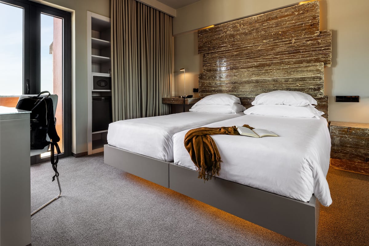 A modern hotel room with a large bed, a wardrobe, a desk, and a view through a glass door.