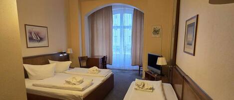 A hotel room with two beds, a desk, a chair, a TV, and a chandelier.