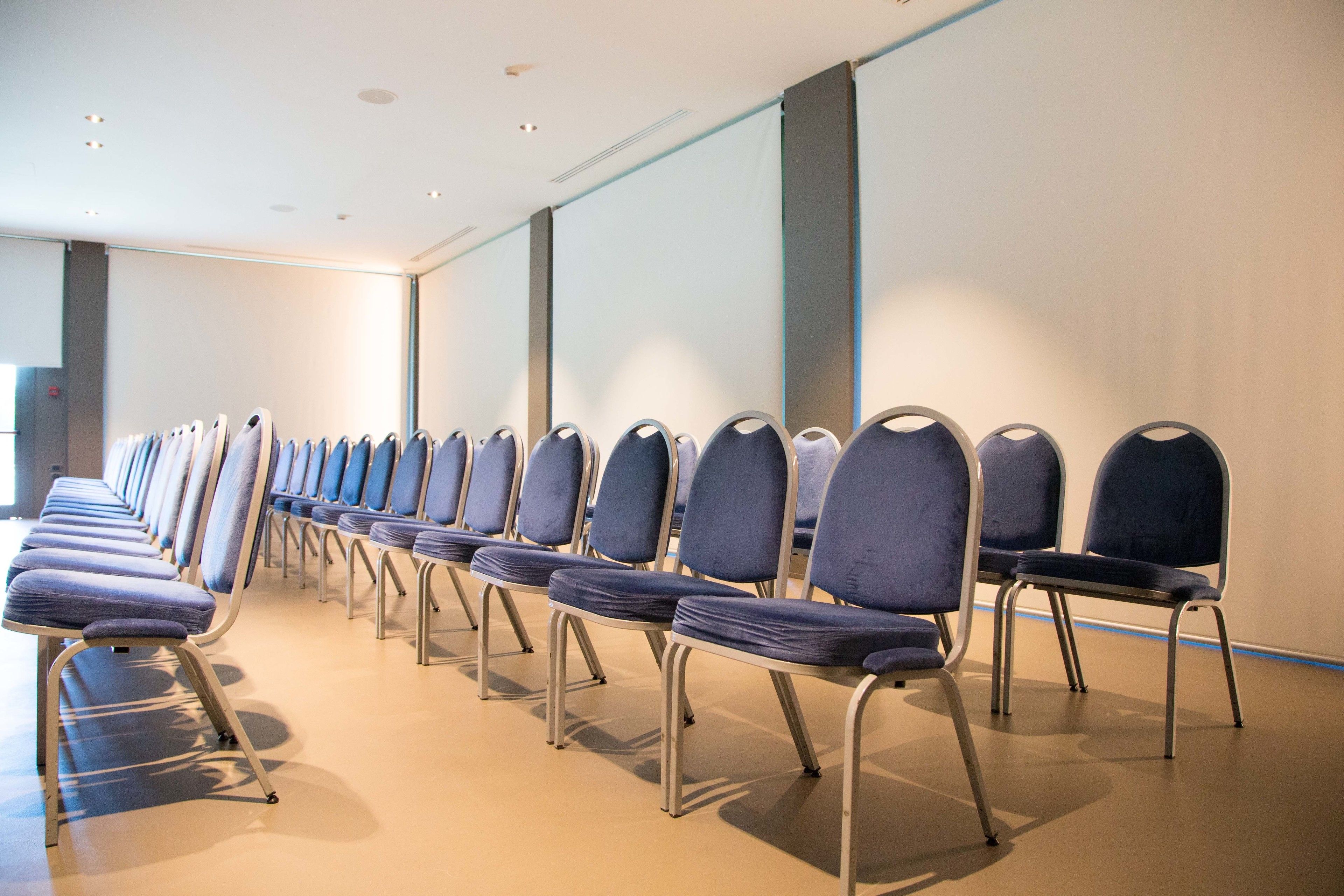 A row of blue chairs with metal frames in a room with a plain wall and a light-colored floor.