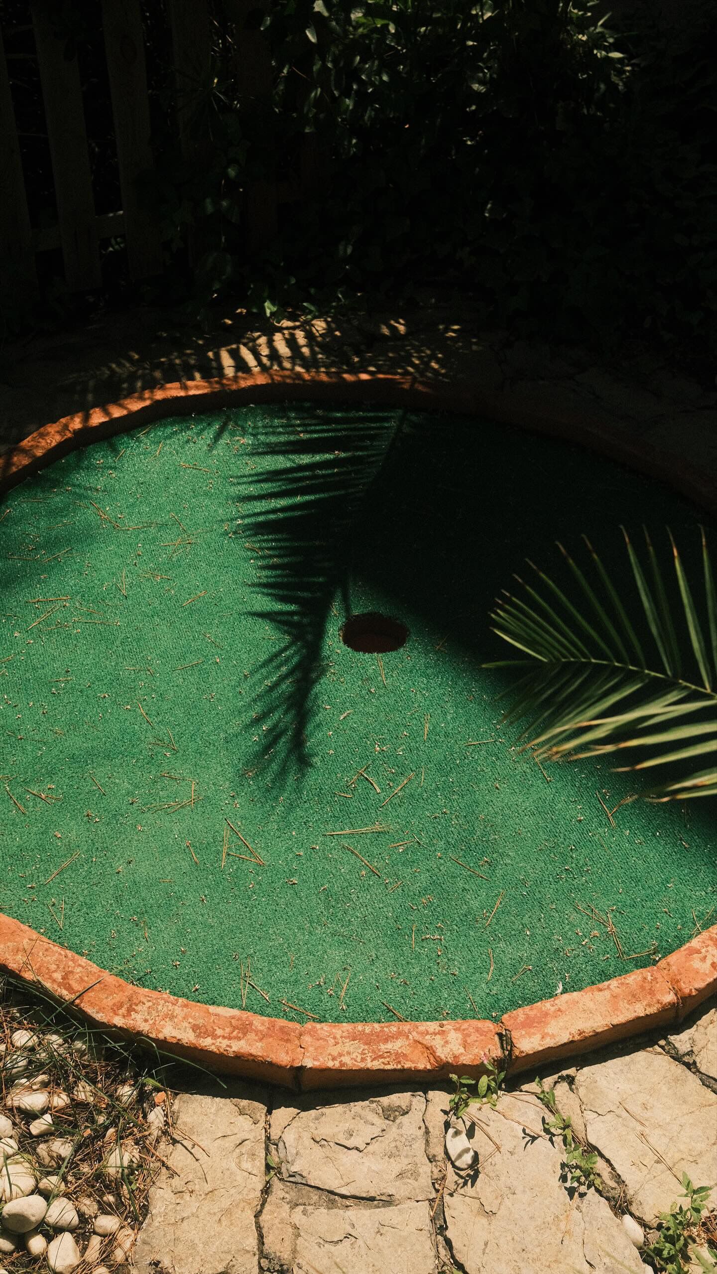 A small, round, green-tiled pool with a brick border, surrounded by rocks and plants.