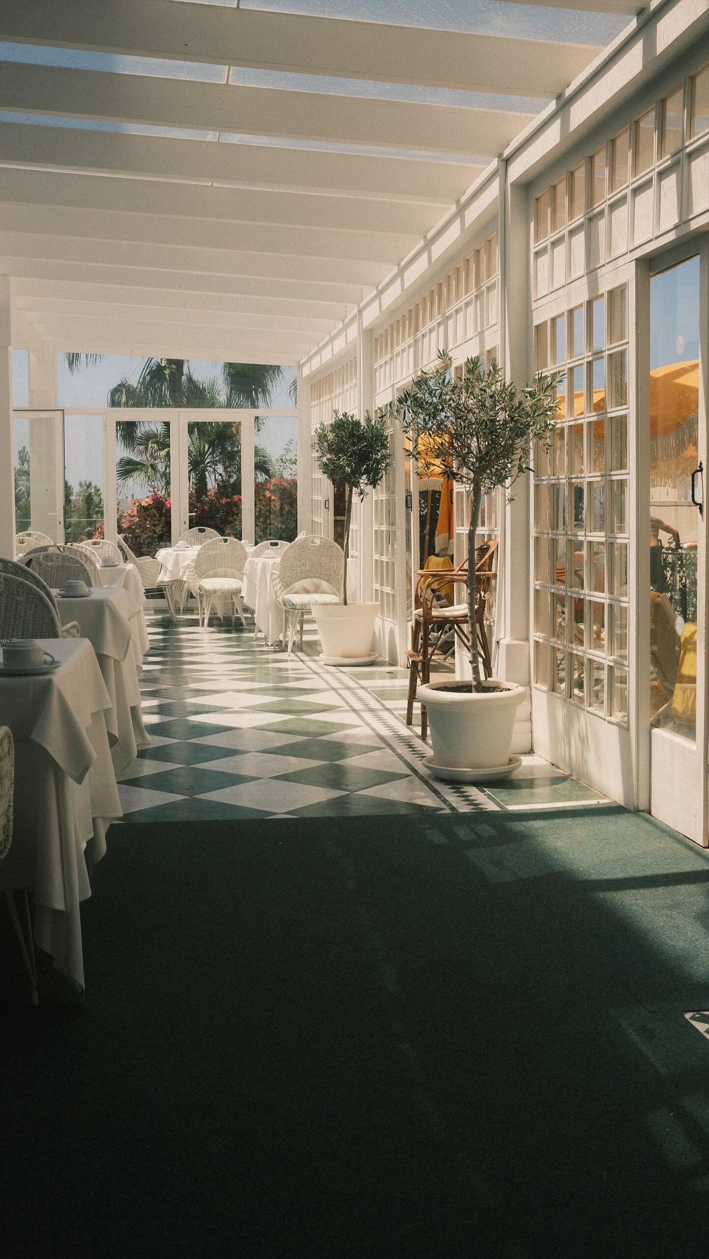 A covered outdoor dining area with tables and chairs, potted plants, and a view of the outdoors.