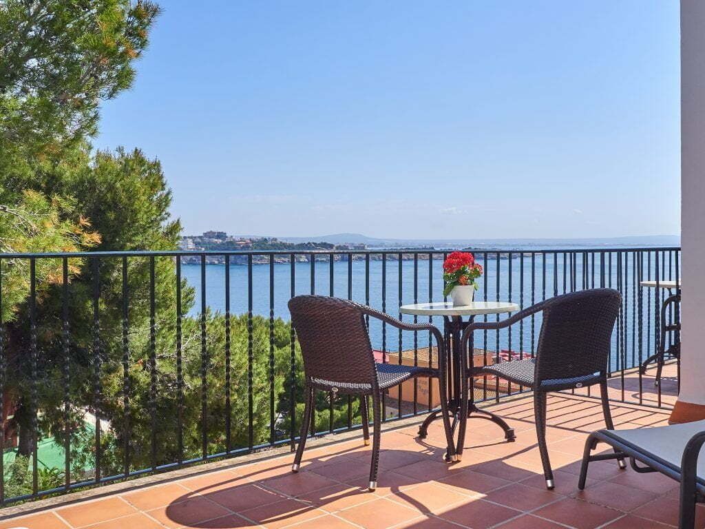 Un balcon avec deux fauteuils en osier et une petite table, d’où l’on peut admirer un plan d’eau et la terre ferme au loin.