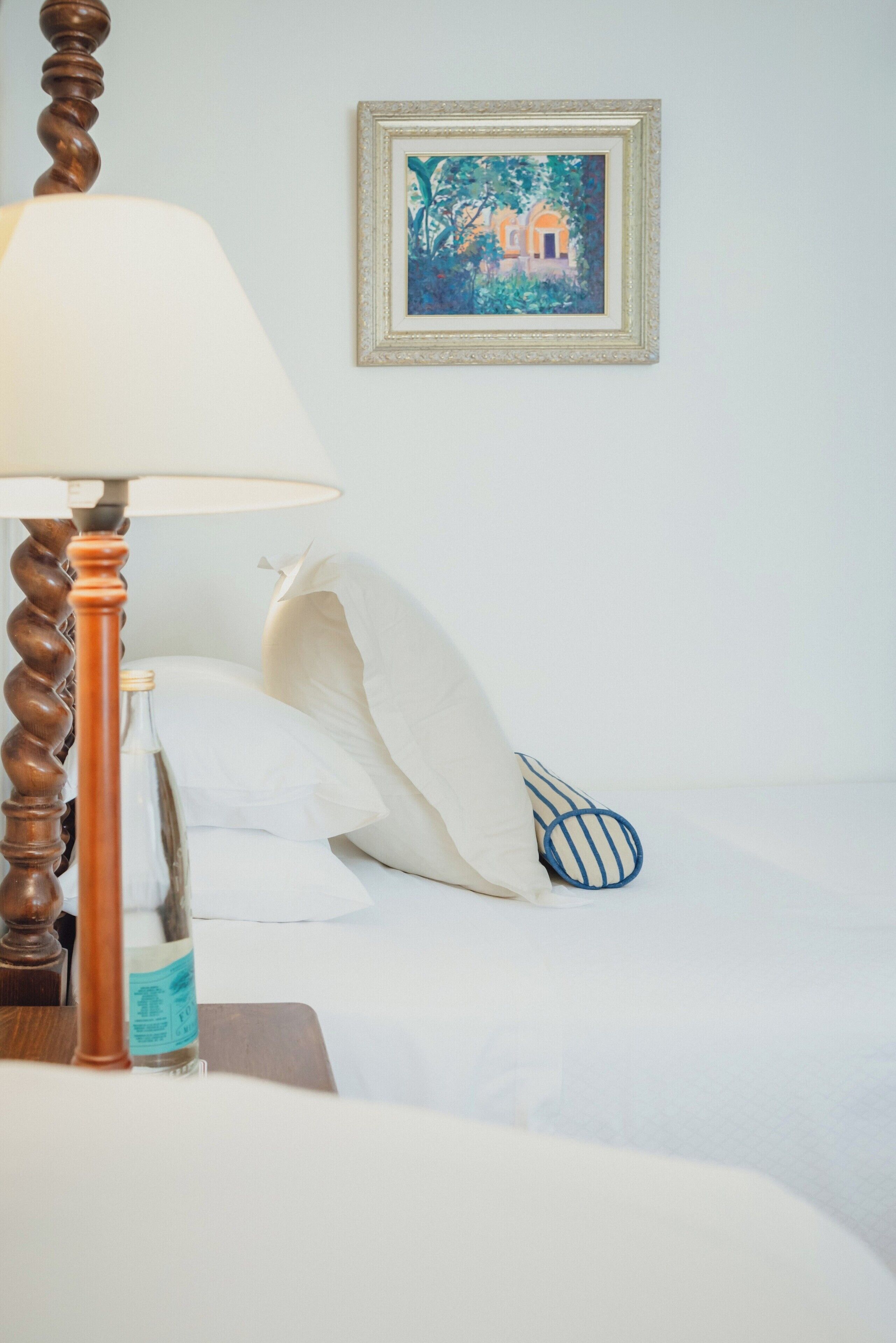 Una habitación de hotel con una cama, una lámpara, una botella y un cuadro enmarcado en la pared.