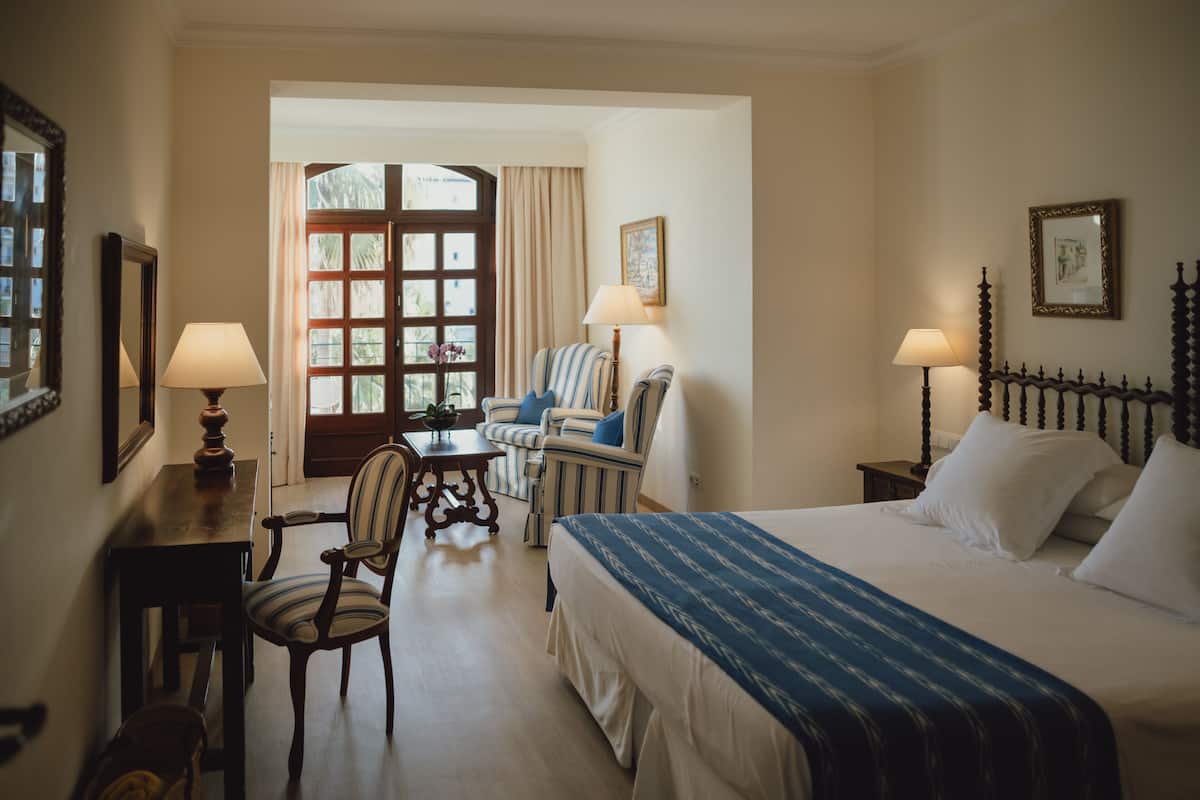 A hotel room with a large bed, a chair, a table, and a window with curtains.