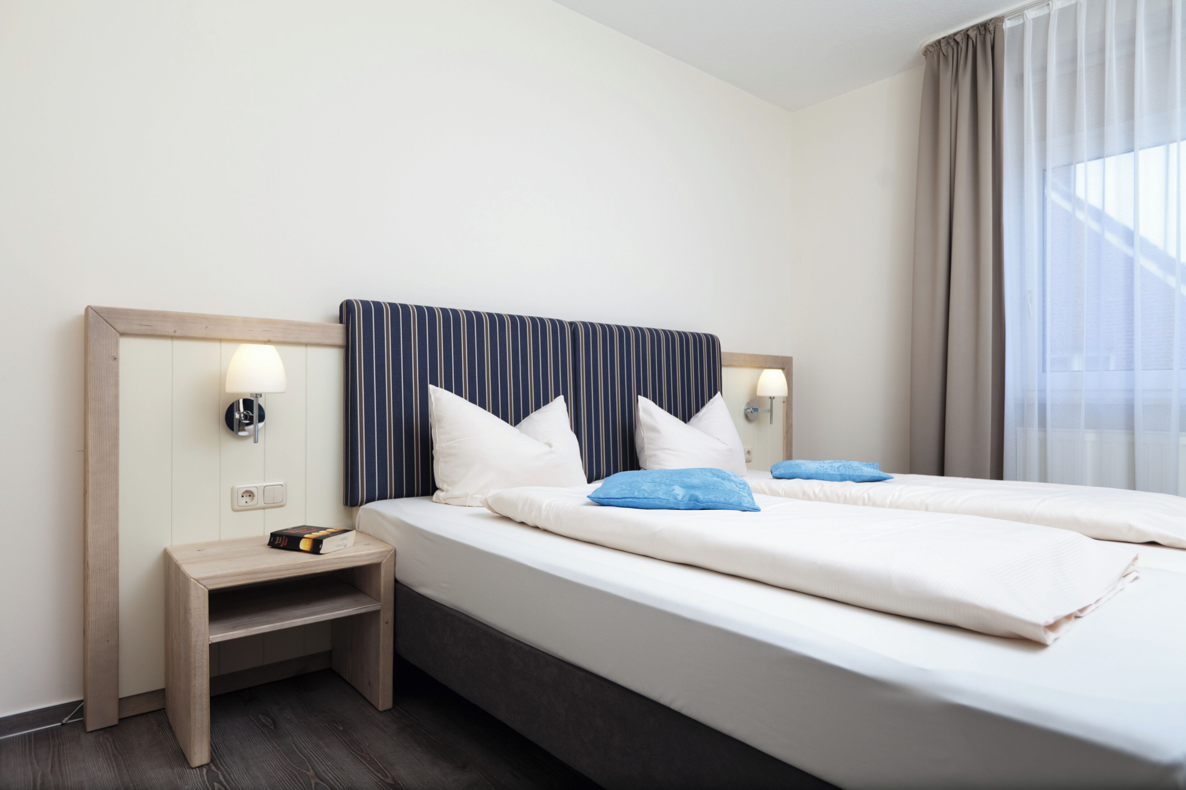 Hotellihuone, jossa on kaksi sänkyä, yöpöytä ja lamppu.