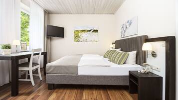 A bedroom with a bed, bedside tables, a desk, a chair, a TV, and artwork on the walls.