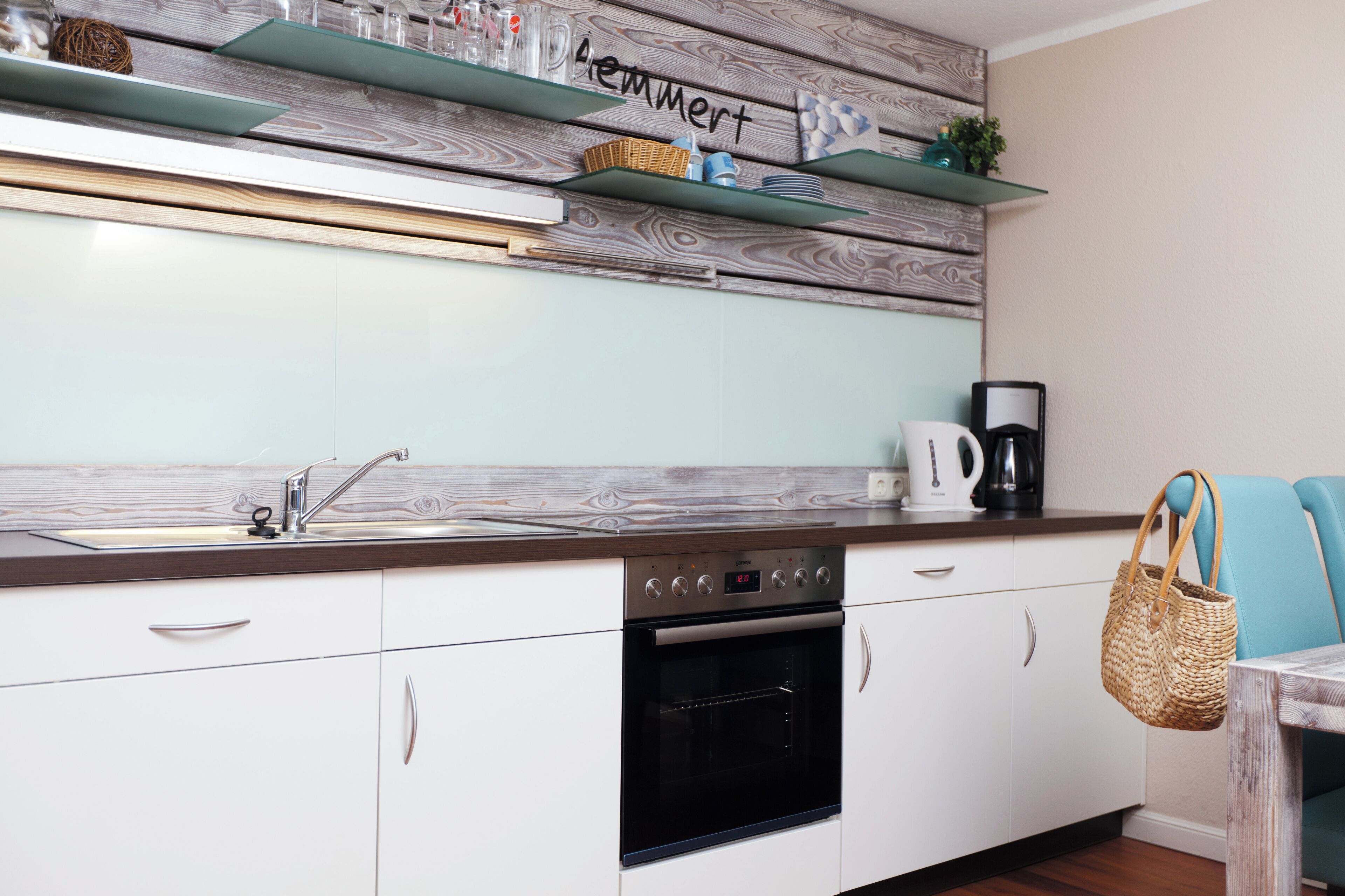 Una cocina con armarios blancos, un horno negro, una cafetera y una cesta de mimbre colgada en la pared.