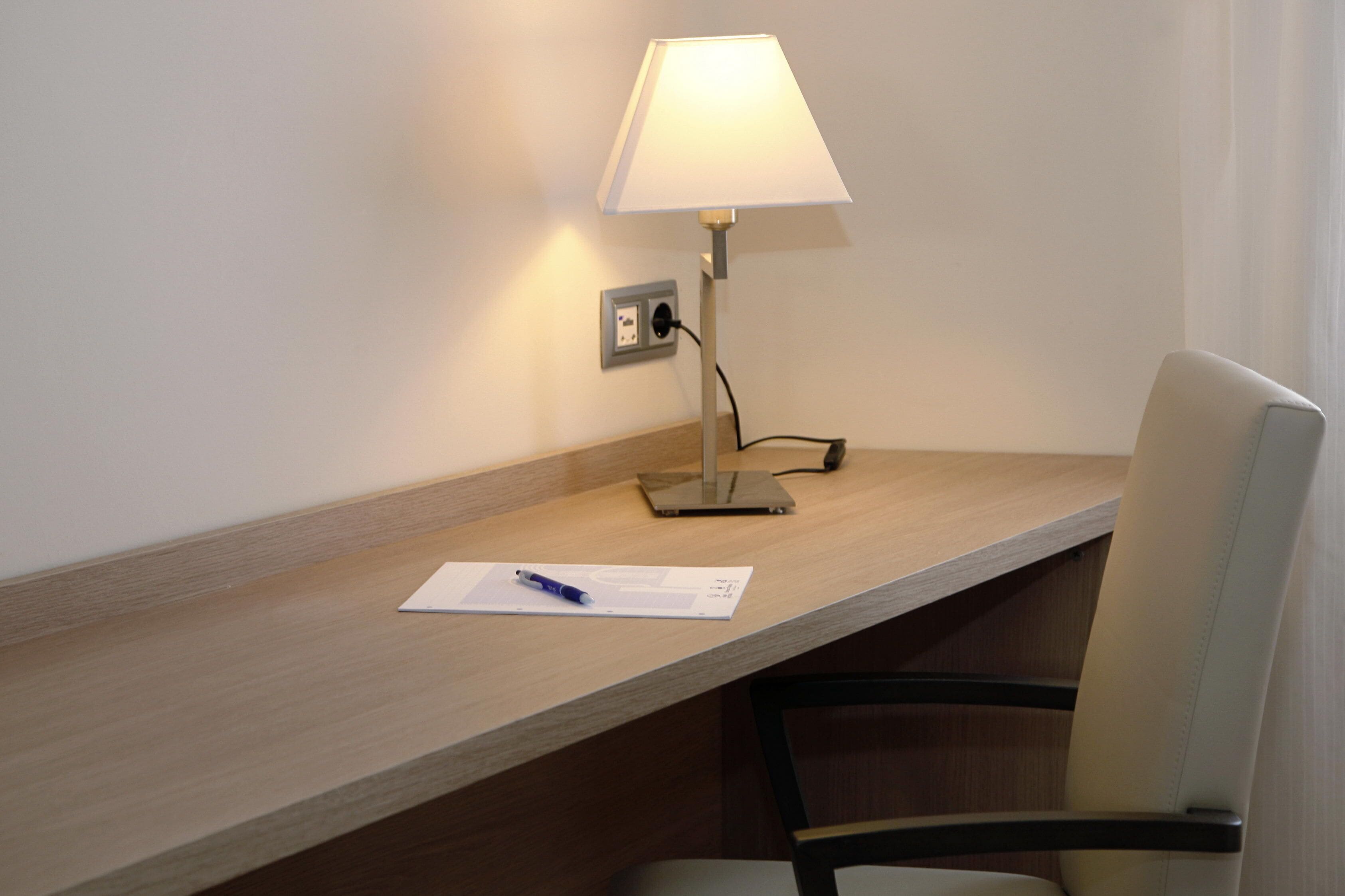 A desk with a lamp, a chair, and a notepad with a pen.