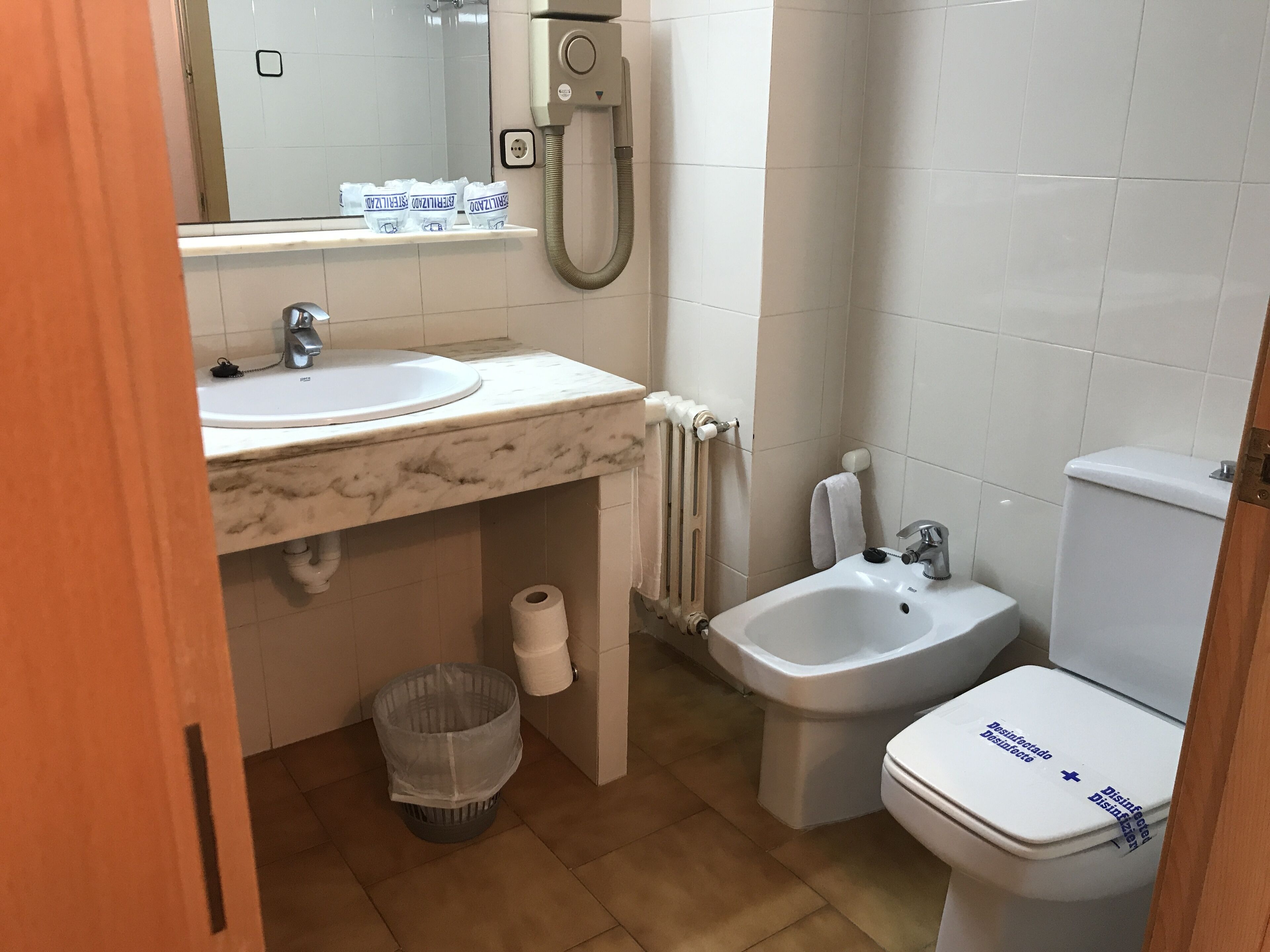 Un baño con lavamanos, bidé, inodoro y un cubo de basura.