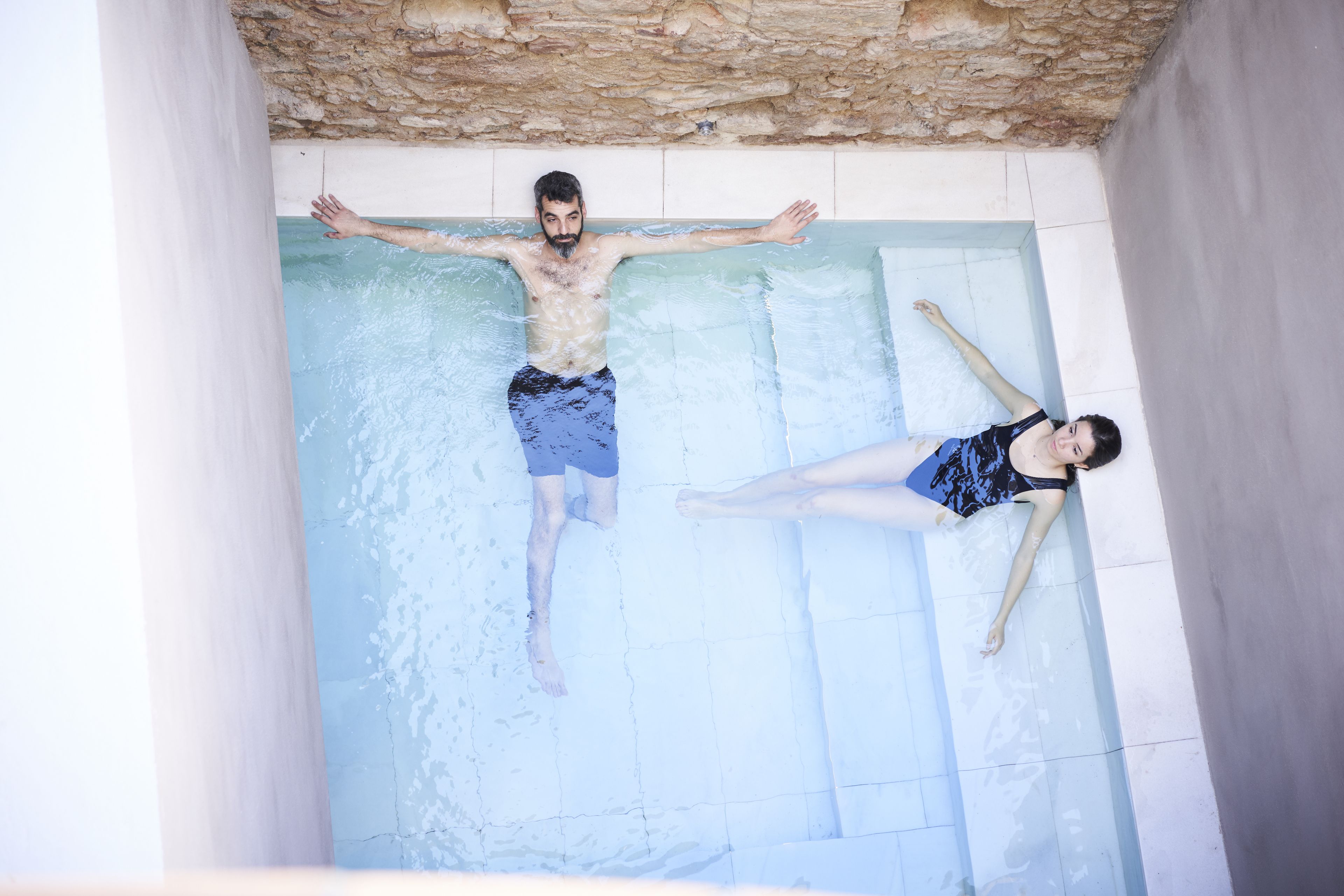 Un hombre y una mujer descansando en una pequeña piscina rectangular con paredes de piedra.