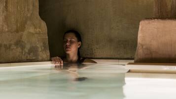 A person in a bathtub with stone walls and a tiled floor.