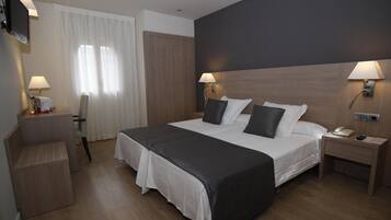 A hotel room with a large bed, bedside tables, a desk, a chair, and a TV on the wall.