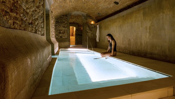 A spa room with a large, rectangular hot tub in the center, surrounded by stone walls and a high, arched ceiling. - Balneari Termes Victòria (Caldes de Montbui)