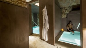 A modern bathroom with a glass-enclosed bathtub, a hanging towel, and a stone wall. - Balneari Termes Victòria (Caldes de Montbui)