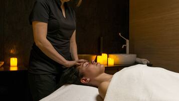 A person receiving a head massage in a dimly lit room with candles, a sink, and a towel.