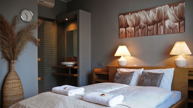 Un lit bien fait, avec des serviettes, une horloge, un vase et un tableau accroché au mur.