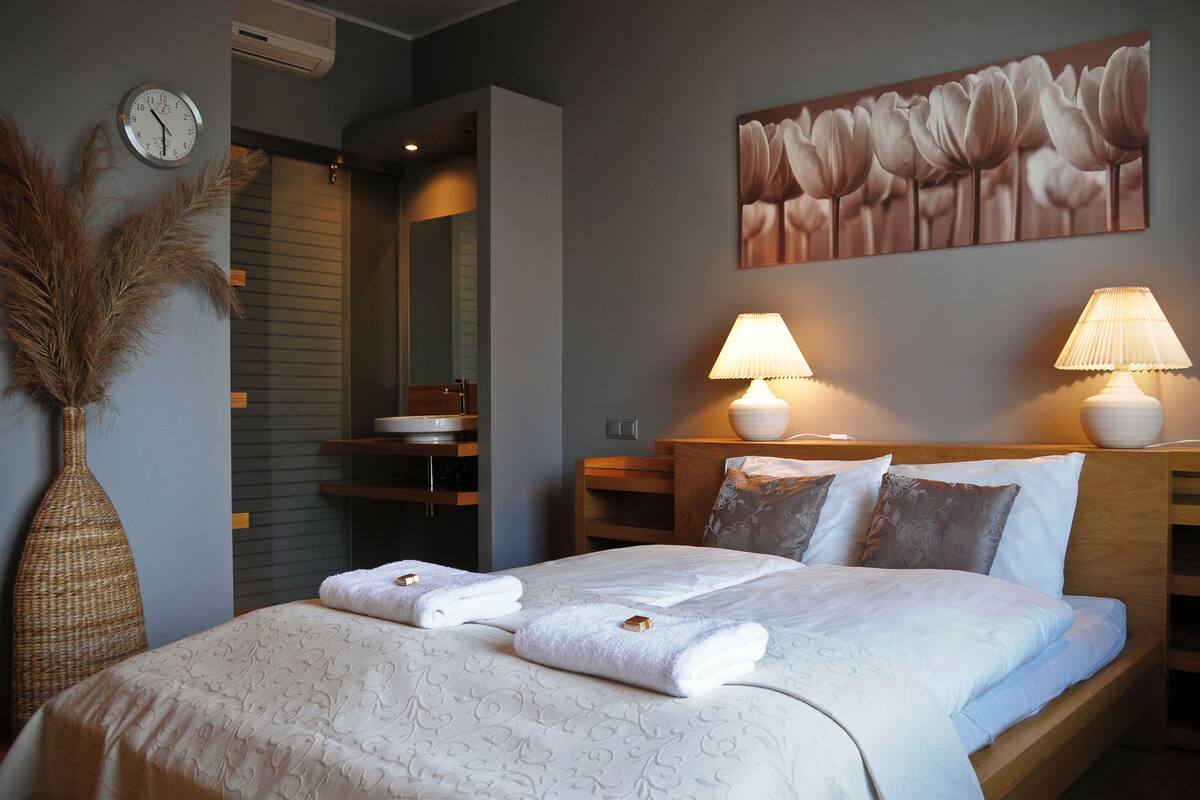 Una cama bien hecha con toallas, un reloj, un jarrón y un cuadro en la pared.