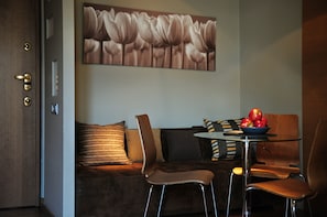 A modern room with a brown sofa, two brown chairs, a glass table with a bowl of apples, and a painting of flowers on the wall.