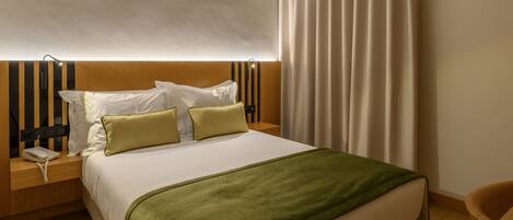 Una habitación de hotel con una cama, una mesita de noche con un teléfono, una lámpara y una cortina.