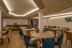A modern dining area with round tables and chairs, a central counter, and a wall-mounted art piece. - Santa Eufémia Covilhã Hotel (Covilhã)