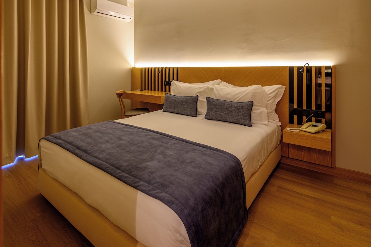 Una habitación de hotel con cama, mesitas de noche, escritorio y teléfono.