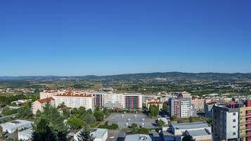 Ein mehrstöckiges Hotel mit Parkplatz im Vordergrund, umgeben von Grünflächen und Blick auf ferne Hügel.