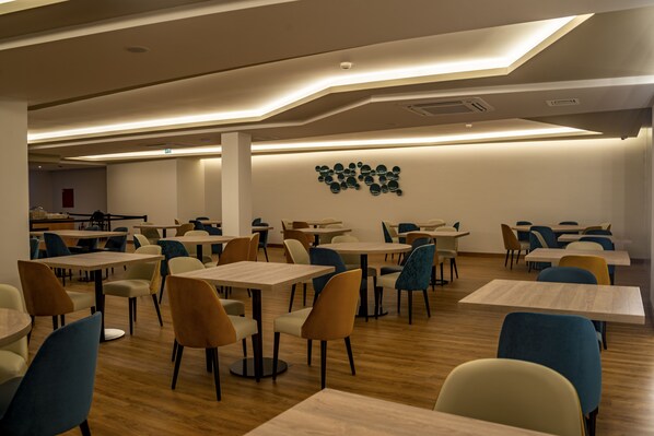 Un vaste espace dédié à la salle à manger, avec plusieurs tables et chaises, un design moderne au niveau du plafond et un luminaire fixé au mur.