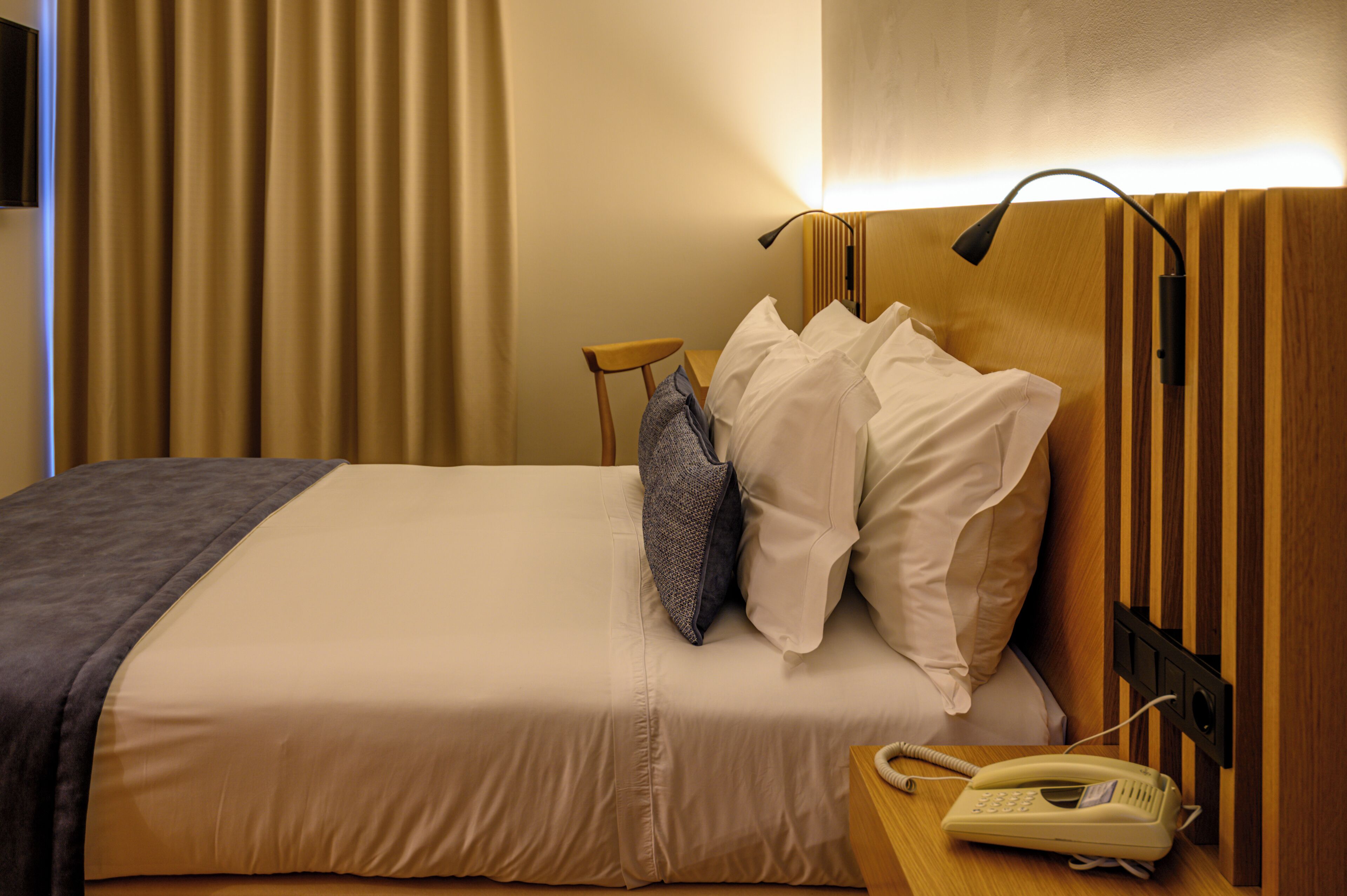 A hotel room with a bed, a bedside table with a telephone, and a lamp.
