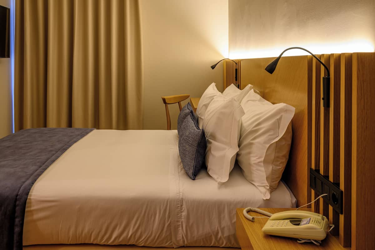 Una habitación de hotel con una cama, una mesita de noche con teléfono y una lámpara.