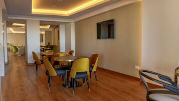 A modern dining area with wooden flooring, yellow and blue chairs, and a flat-screen TV mounted on the wall.