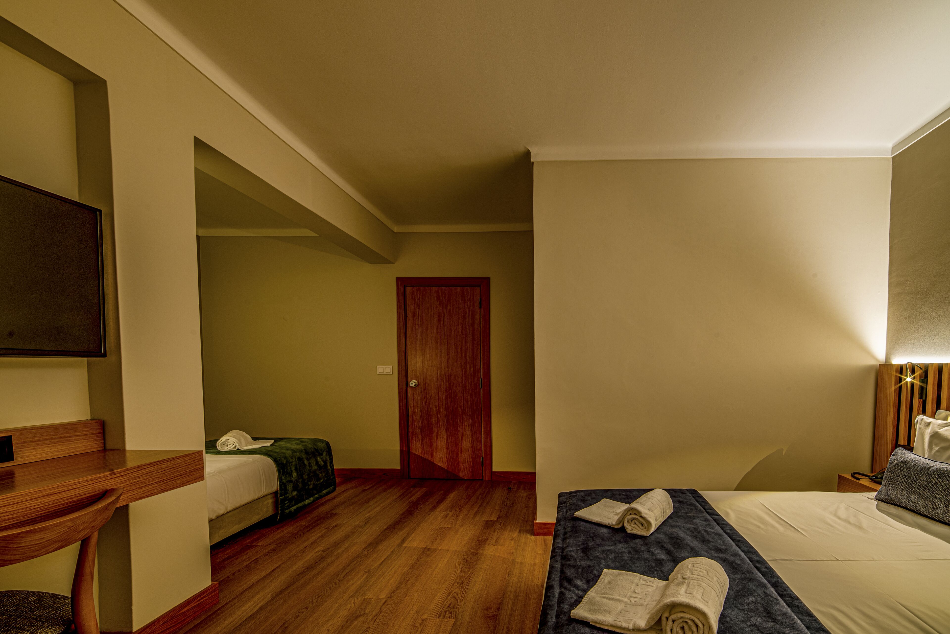 A hotel room with a bed, a desk, a chair, a television, and a door.